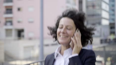 mujer de negocios sonriente hablando por teléfono mientras camina por la calle