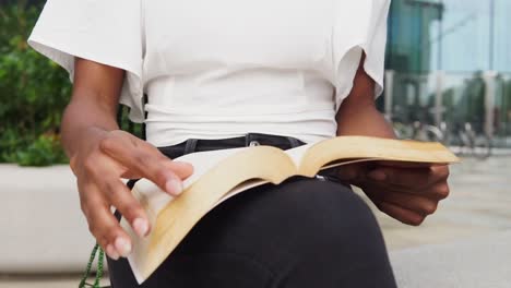 mujer negra anónima leyendo un libro en la calle