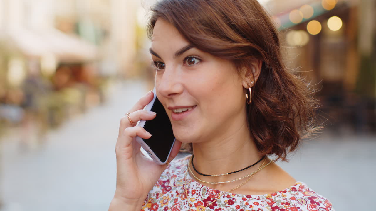 Happy young woman having remote conversation talking on smartphone good news gossip in city street