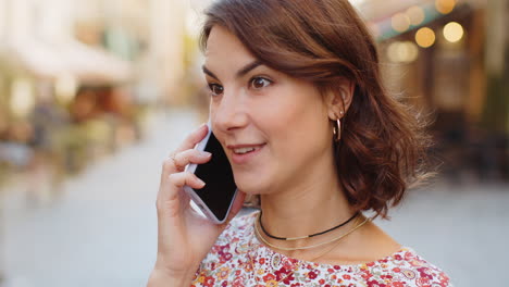 happy young woman having remote conversation talking on smartphone good news gossip in city street