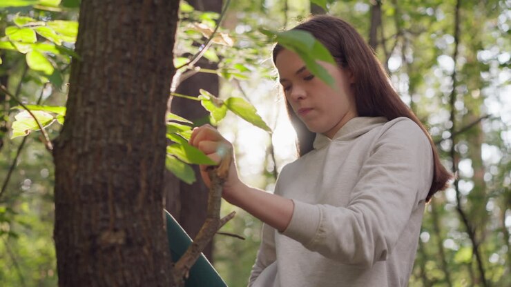 Woman stretches leg using tree branch to put foot in forest. Young lady performs intentional stretching exercises to ease tension after jogging at sunset