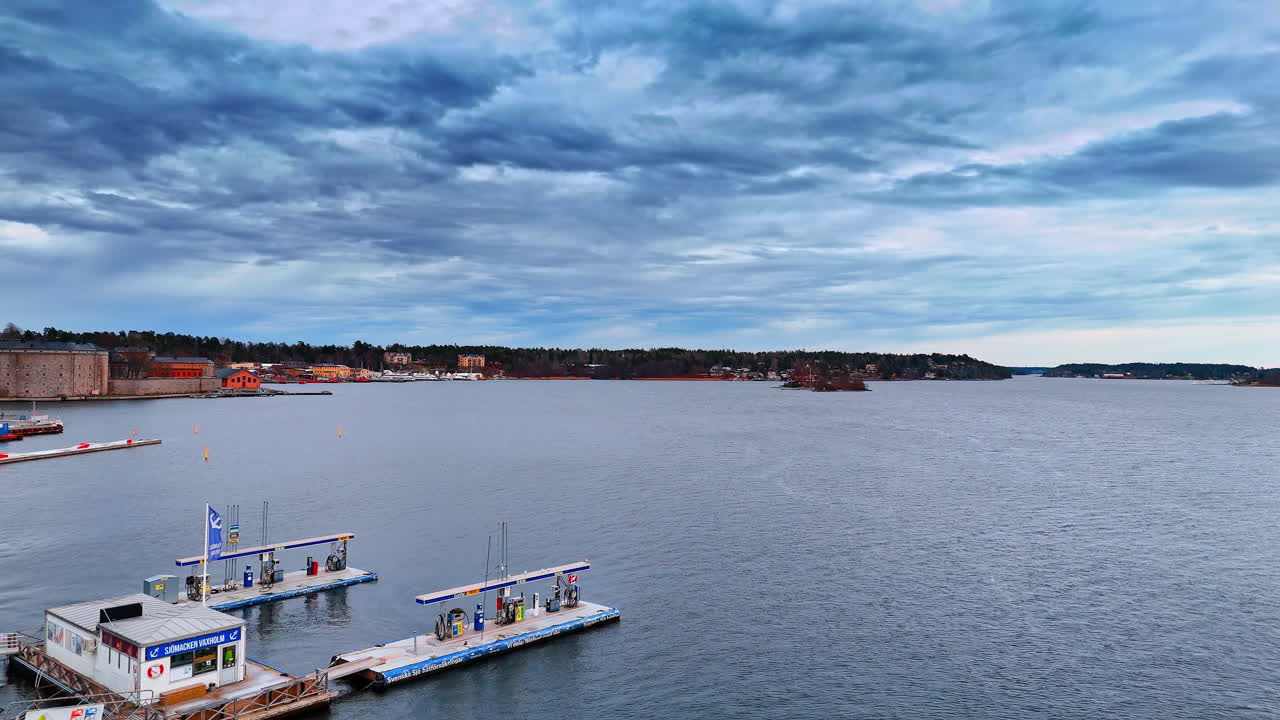 Stoccolma, Svezia, 25 dicembre 2025: Salendo sopra l'ormeggio sopra il paesaggio acquatico opaco che riflette un cielo nuvoloso e drammatico. Vista rivelatrice sulla stazione di servizio galleggiante per barche a Vaxholm, Svezia.