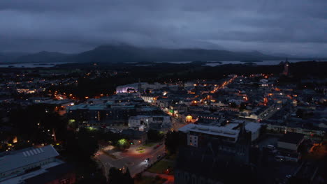 Aerial-panoramic-footage-of-evening-town-and-mountains-around-lake-in-distance.-Illuminated-streets.-Killarney,-Ireland