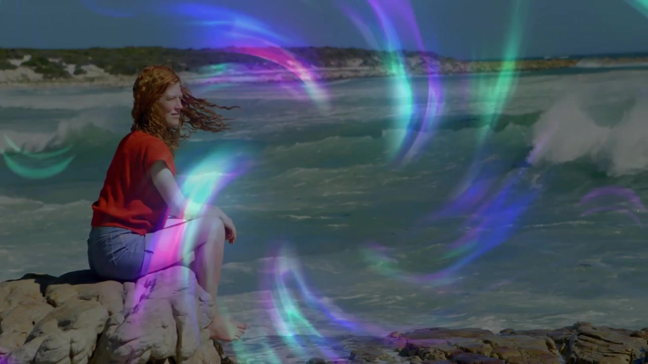 Donna seduta su una roccia di fronte al mare, con un vortice digitale che appare, avvolge la donna e poi svanisce per una demo tecnologica.