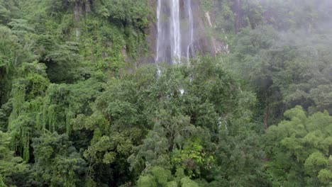 aerial rising over green dense rainforest and clouds revealing las lajas misty waterfall, san luis morete, costa rica