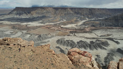 Vista-Aérea-De-Una-Mujer-Caminando-Hasta-El-Borde-Del-Acantilado-Sobre-El-Abismo-Y-El-Cañón-Del-Desierto-Seco,-Utah,-EE.UU.