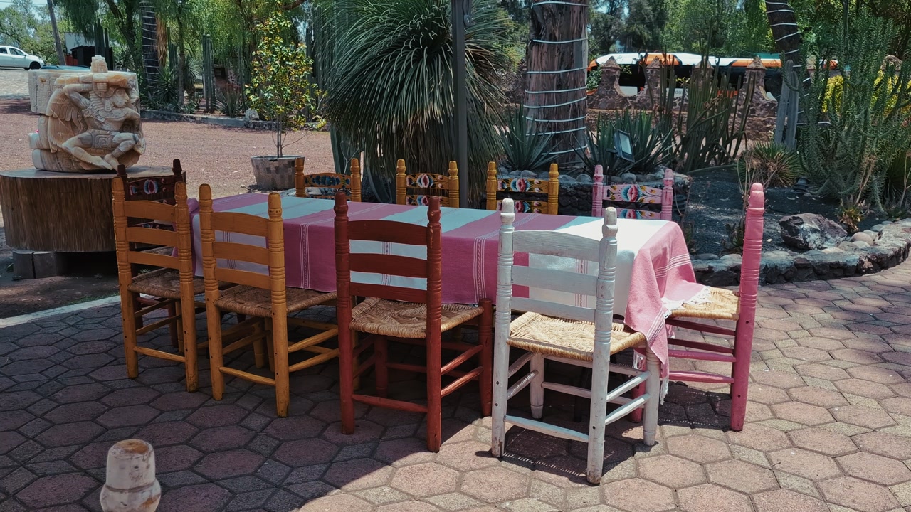 Colorful wooden chairs around a table with pink cloth in an outdoor setting in Mexico. Vibrant local design, rustic charm, and traditional atmosphere.