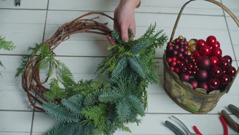 Making rustic christmas wreath. Hands holding green branches on rustic wooden background. Seasonal holiday workshop online, making festive decorations at home