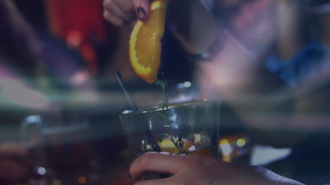Mani di una cliente che raccolgono un'erba e abbassano una fetta d'arancia in un cocktail, mescolando la guarnizione sul bancone del bar.