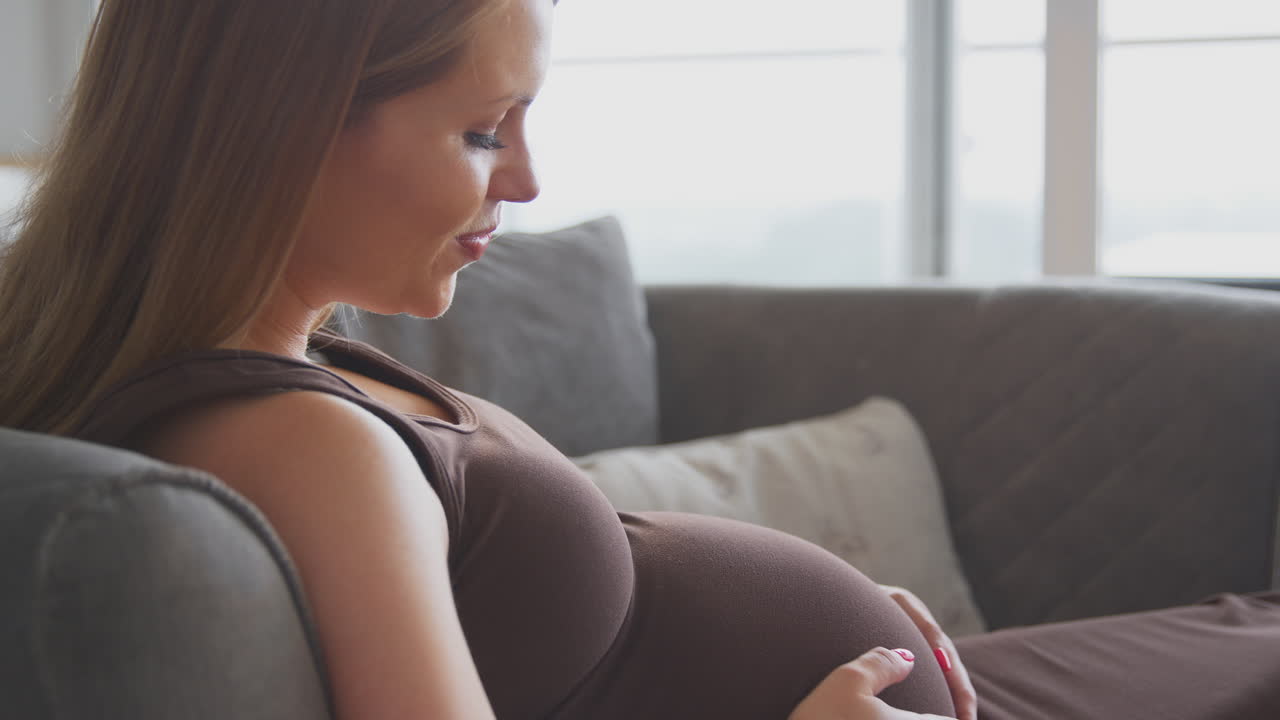 임신 한 여자 가 집 에서 소파 에서 휴식을 취 하고 배 를 들고 아기 와 대화 하고 있다