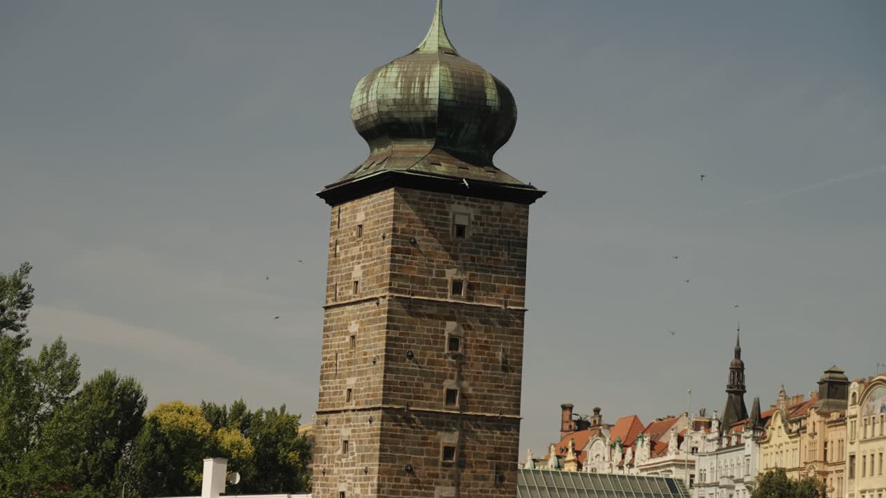 Stone tower with green copper dome and birds flying above trees in Prague