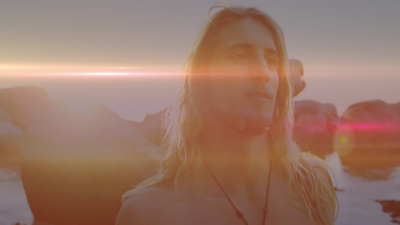 La telecamera inquadra da vicino un uomo a torso nudo con una collana in uno spot di viaggi, la costa si rivela sotto il bagliore dell'obiettivo