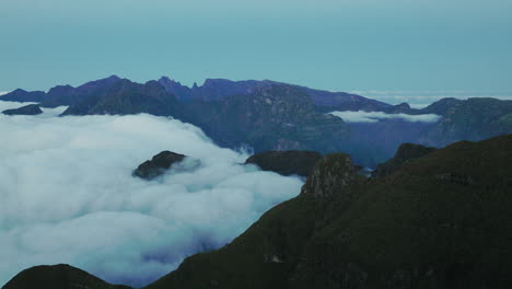drone view of clouds flowing down mountain plateau to lower valley