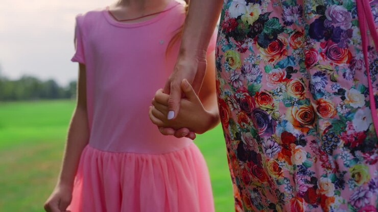 Unrecognizable woman and girl enjoying summer evening in city park at sunset