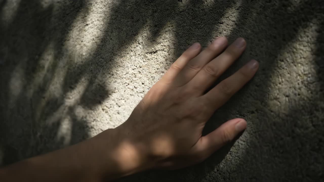 Human Hand Gently Touching Textured Surface with Moving Sunlight and Shadows