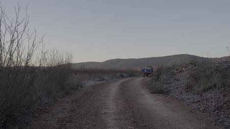 Man-driving-tractor-on-rural-road-between-dry-fields