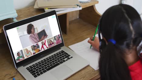 Schoolgirl-using-laptop-for-online-lesson-at-home,-with-diverse-teacher-and-class-on-screen