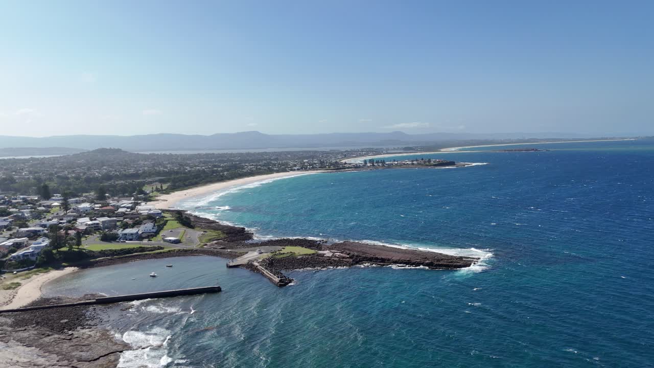 Coastal aerial establishing of Shellharbour jetty and surrounding sea in early daylight, white sandy beach stretch