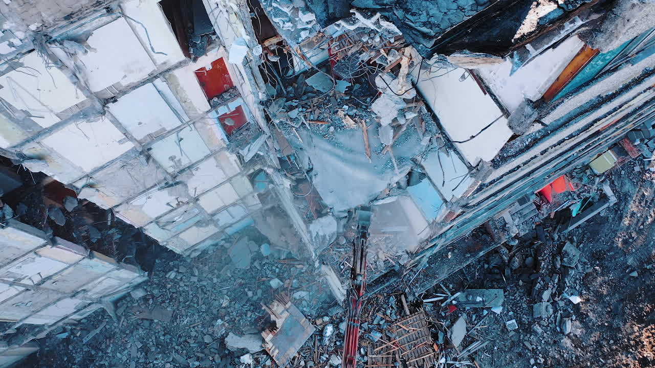 Excavator riches high to demolish floors and walls of a concrete structure. Broken pieces of concrete falling on the ground with the clouds of dust.