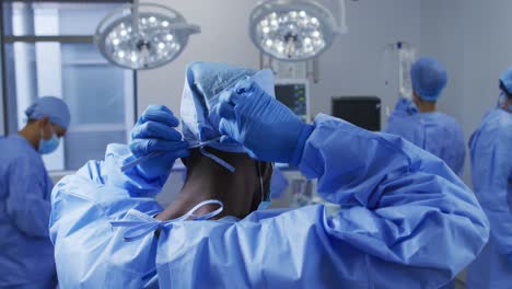 African-american-male-surgeon-putting-on-protective-clothes-standing-in-operating-theatre