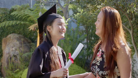 graduating, young woman in cap and gown receiving diploma from asian mother