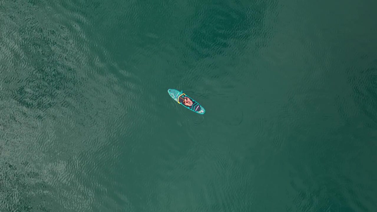 Vista aerea dall'alto di una donna sola che fa paddleboard in un vasto paesaggio lacustre con acqua blu