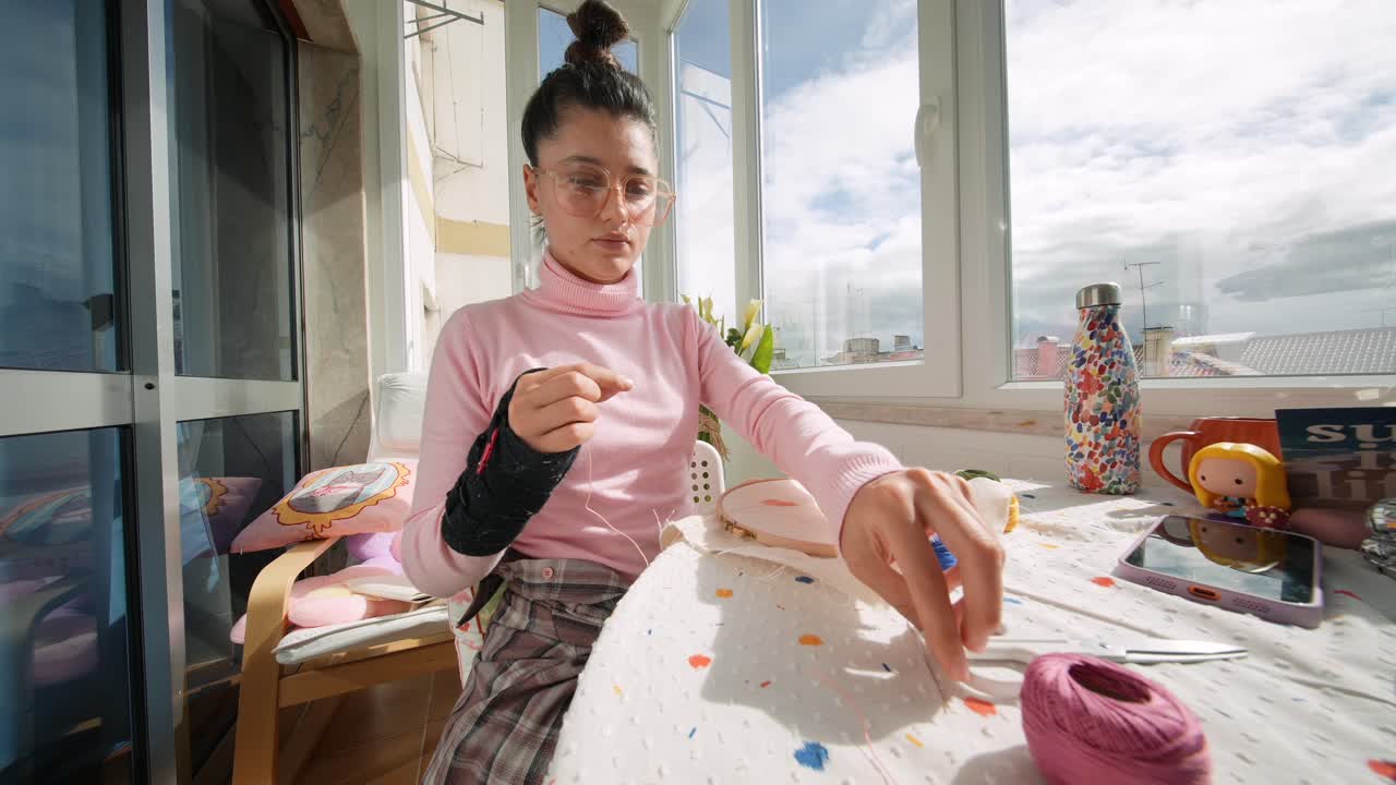 Giovane donna con tutore al polso che ricama a casa