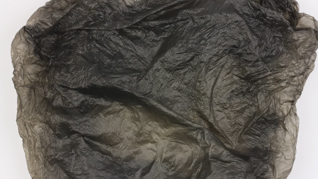 bagagem de plástico preta usada gira em fundo branco e se expande para tela completa, close-up, loop de vídeo, animação stopmotion, problema de poluição de lixo