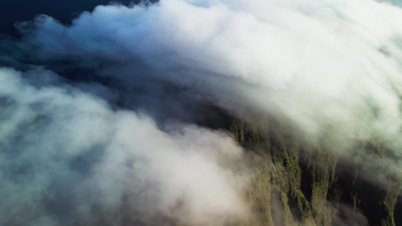 Schnell ziehende Wolken mit dichter Wolkendecke über einem Gebirgskamm bei Tageslicht, die grüne Hänge darunter bedecken und dramatische Luftaufnahmen einer Landschaft per Drohne erzeugen