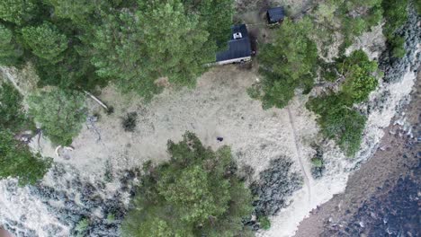 Aerial-drone-footage-rising-above-frozen-Scots-pine-trees-and-Bob-Scott's-Bothy-in-a-frozen-winter-landscape-with-a-fast-flowing-water