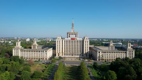 rotating aerial view of the house of the free in bucharest, romania, surrounded lush vegetation and a clear blue sky in the background