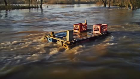 A makeshift raft carrying crates drifts on rapidly flowing waters, showcasing the power of nature and human ingenuity as it navigates the tumultuous river currents.