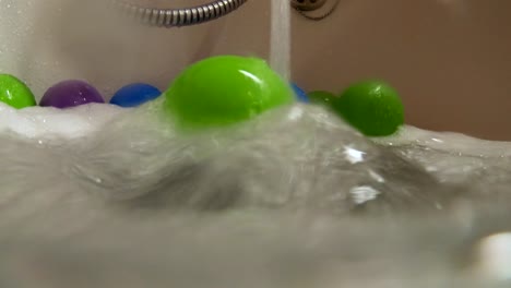 green plastic ball rolled by water stream in bath tub, slow motion, colorful home scene, relaxing bubble bath for children, childhood concept, underwater shot