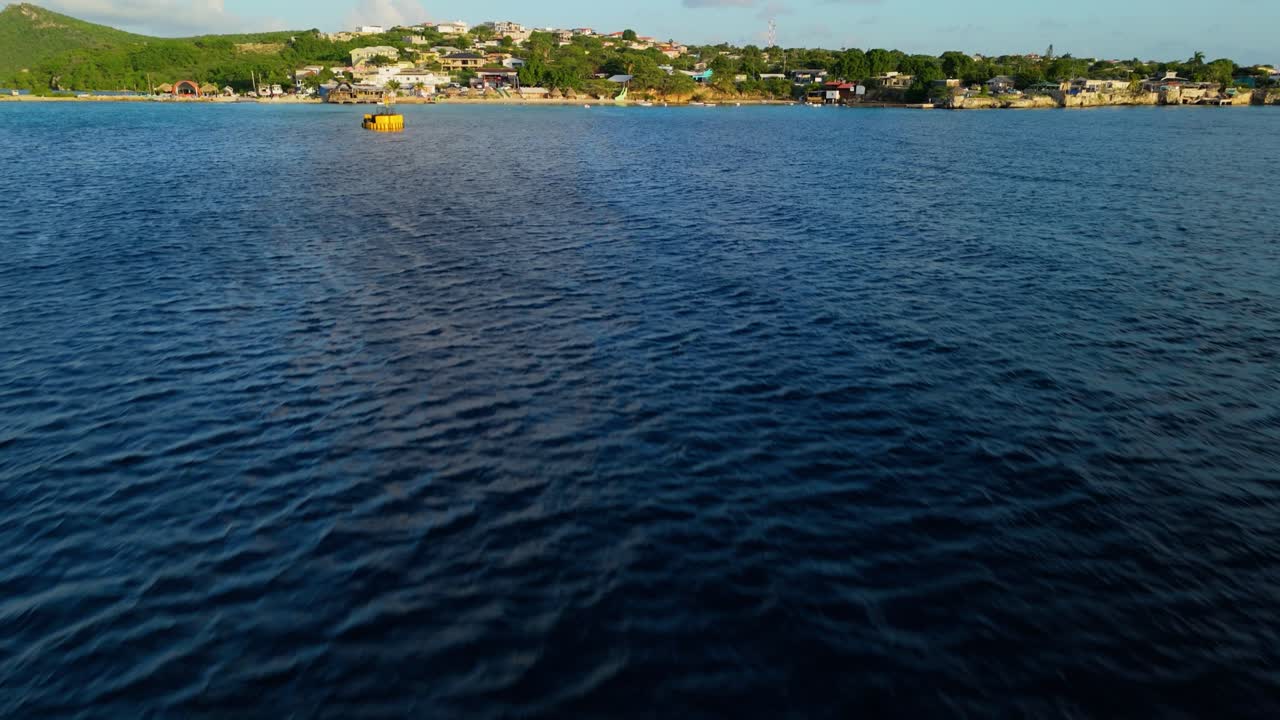 Drone in tilt-up da un epico raggio di luce che si estende sull'oceano aperto, verso un piccolo villaggio di pescatori caraibico