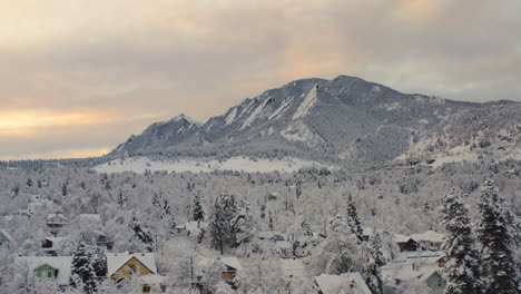 low drone shot moving forward of boulder colorado and rocky flatiron mountains after large winter snow storm covers trees, homes, streets, and neighborhood in fresh white snow