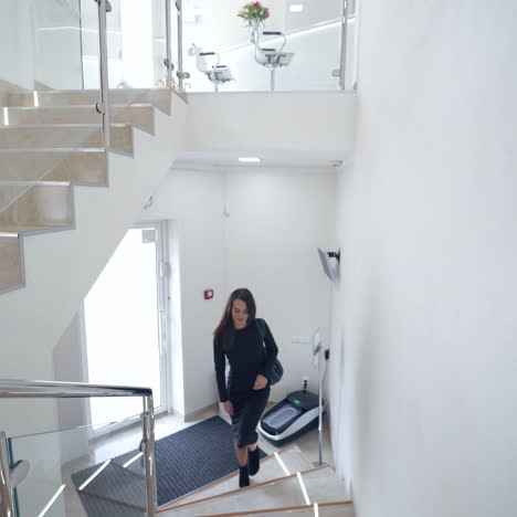 pretty female in black dress inside the light building. young beautiful business woman is going upstairs in a business center or in a hotel.