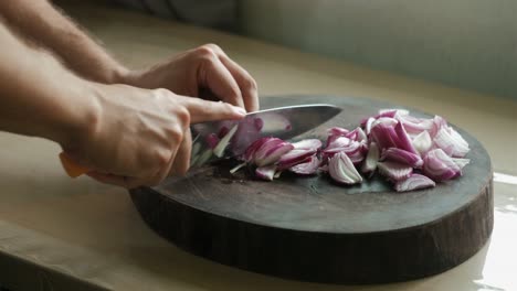 static close-up shot of hands cutting red onions on a wooden chopping board.