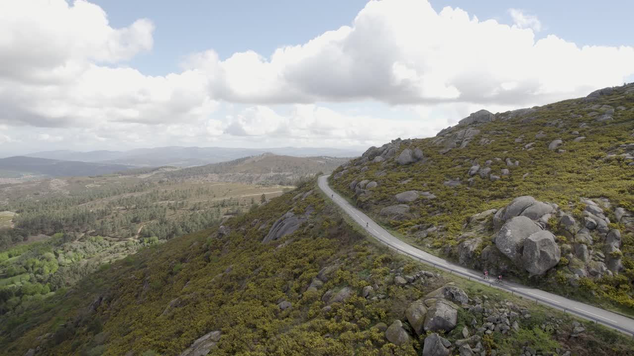 Cyclists riding against sweeping Serra D’Arga slopes as a winding road cuts through rugged peaks in northern Portugal