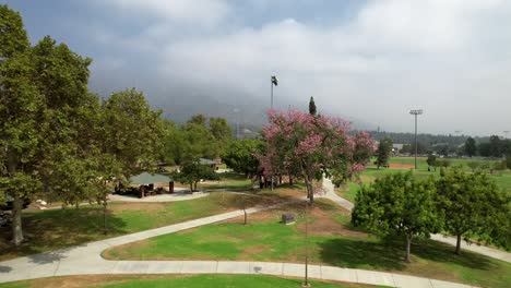 Vista-Aérea-Del-Parque-Recreativo-Público-De-Pasadena-Brillante-Y-Soleado-Que-Se-Eleva-Al-Horizonte-De-La-Montaña-Brumosa-En-La-Distancia