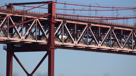 a passenger train passing below the road way on the abril suspension bridge in portugal - close up shot