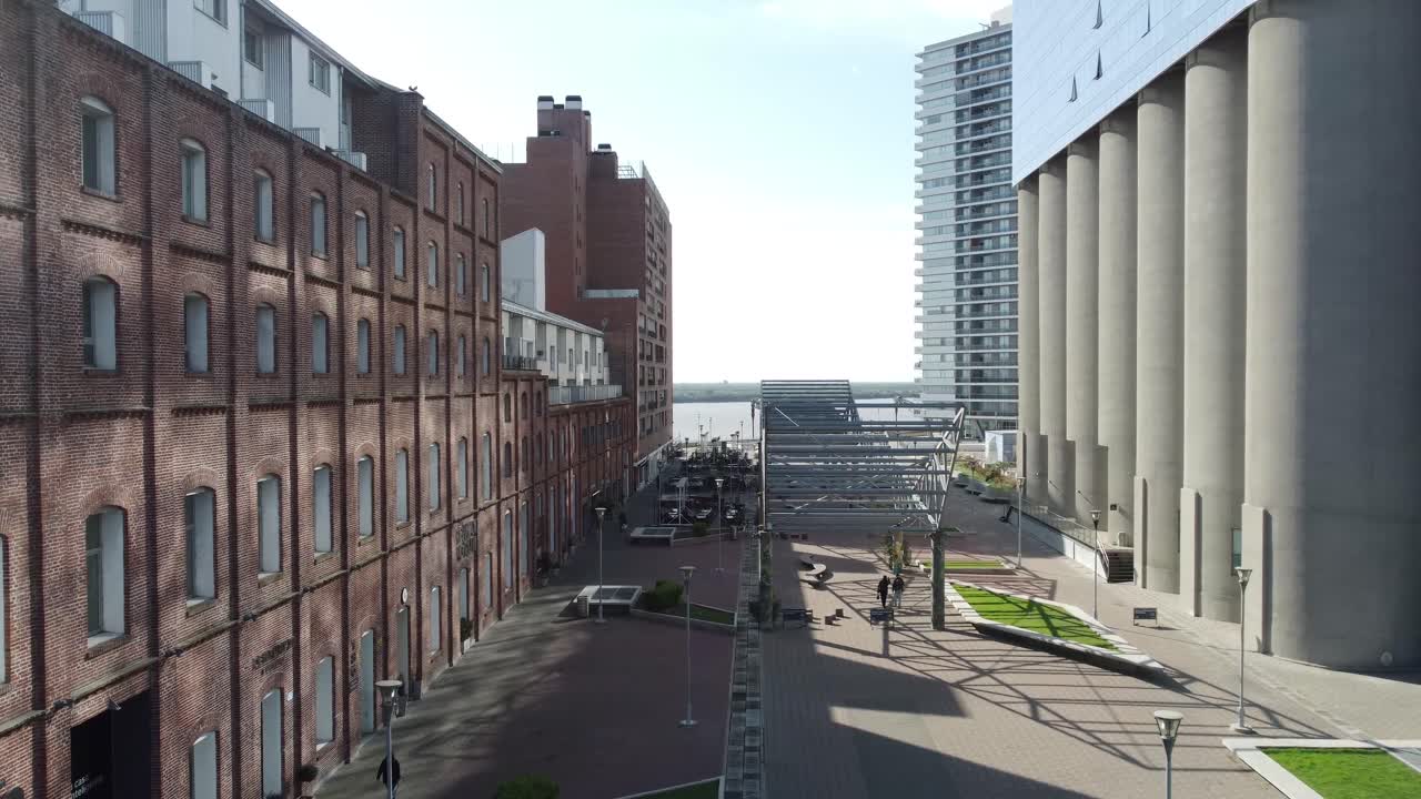 A drone captures an urban landscape featuring a contrast between an old building and modern structures surrounding a dry plaza, showcasing the blend of historic and contemporary architecture.