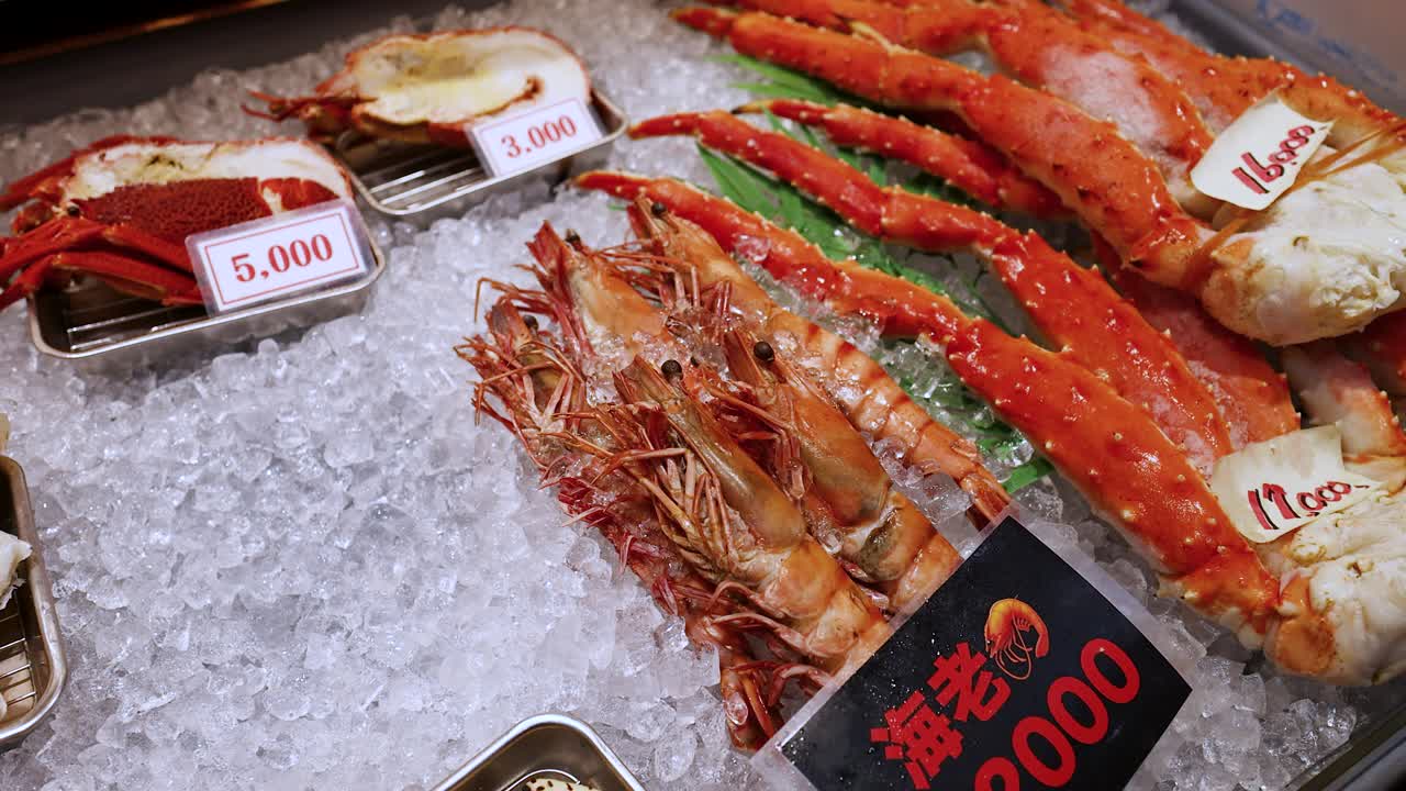 Close-up panning shot of fresh king crab legs and large prawns displayed on crushed ice