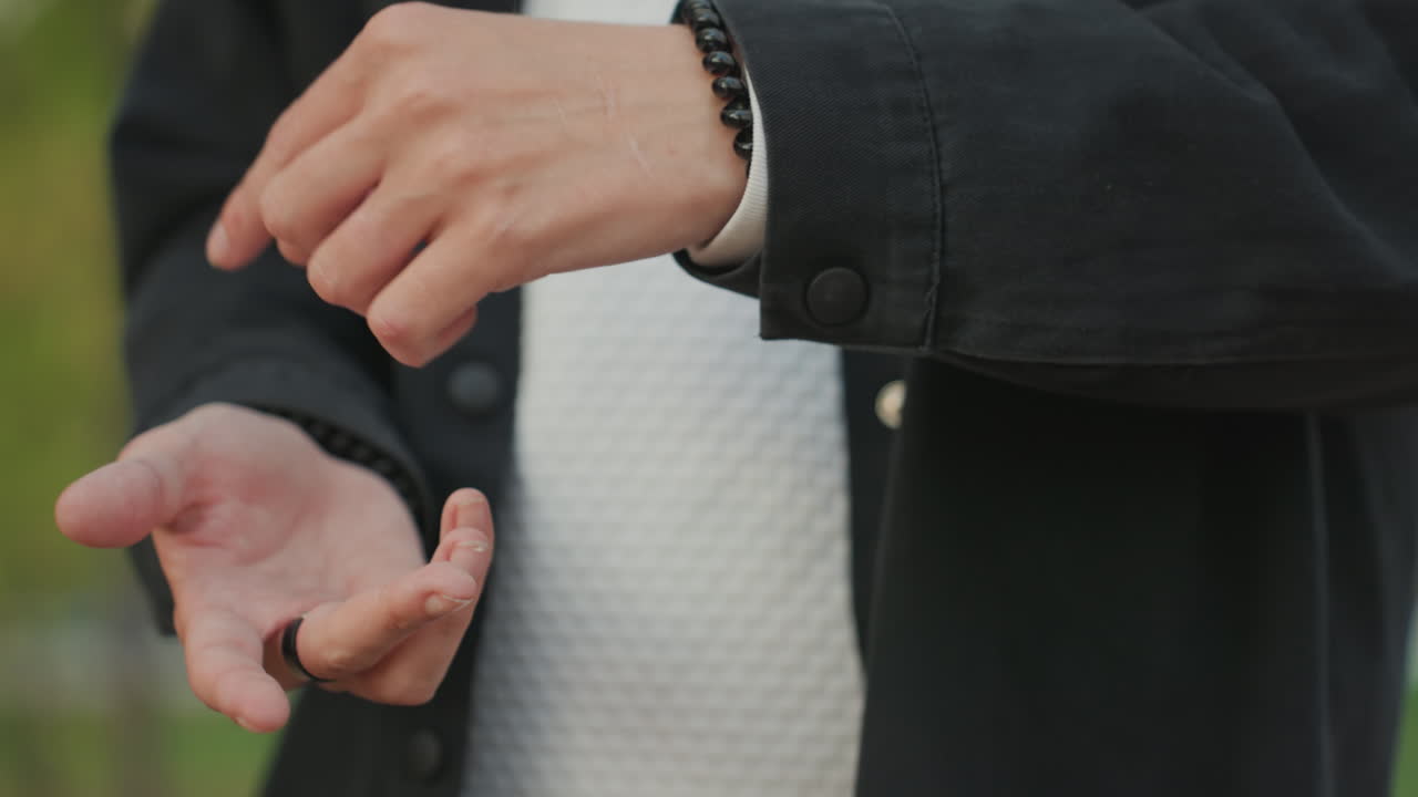 結婚指輪を持つ手のクローズアップ。新郎となる男性が緊張しながら指輪を調整し、指が震える。カフスとブレスレットが見え、金属の輝きと肌の質感がマクロで捉えられた、誓いの象徴的な瞬間。