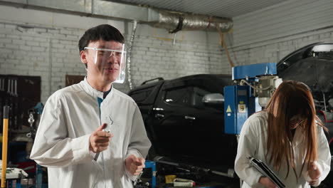 dos estudiantes con abrigos de laboratorio blancos y gafas protectoras bailando juntos en un taller mecánico, con la luz creando un efecto silueta, capturando un momento animado y divertido en un entorno industrial