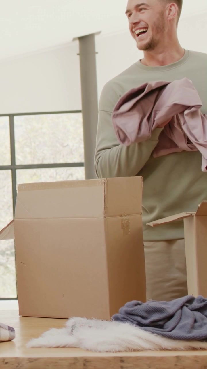 Video vertical: Abriendo una caja de donaciones, un hombre con camiseta verde dobla ropa en una mesa preparando donaciones.