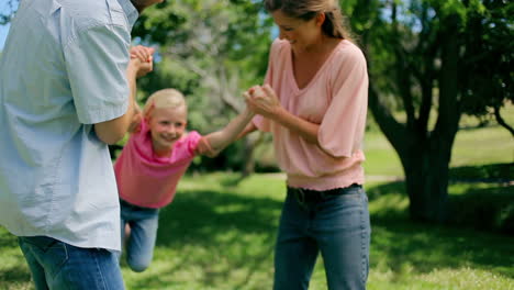 niña siendo balanceada hacia adelante y hacia atrás por sus padres que la están sosteniendo en los brazos