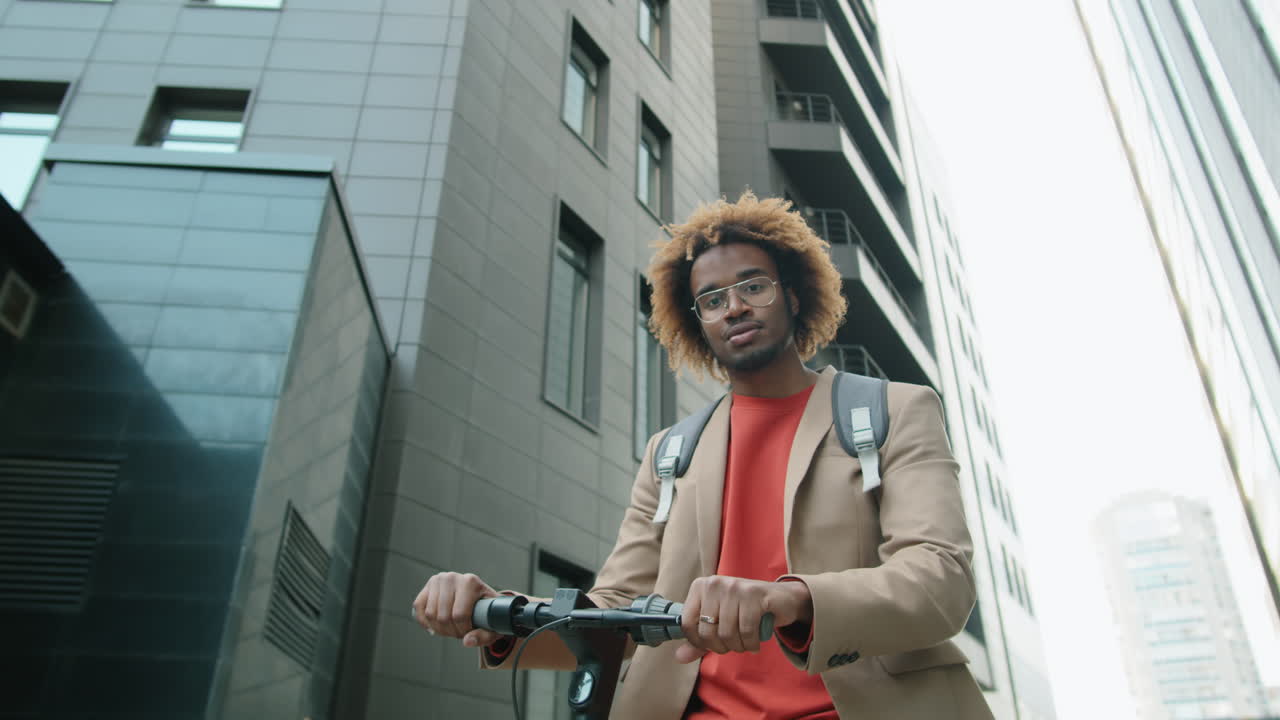 Porträt eines fröhlichen afroamerikanischen Mannes, der mit einem E-Scooter in der Stadt steht
