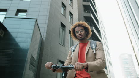 portrait of cheerful african american man standing with e-scooter in city