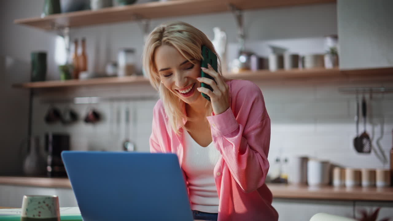 Freelancer multitasking che parla al telefono e scrive al computer portatile in cucina, primo piano