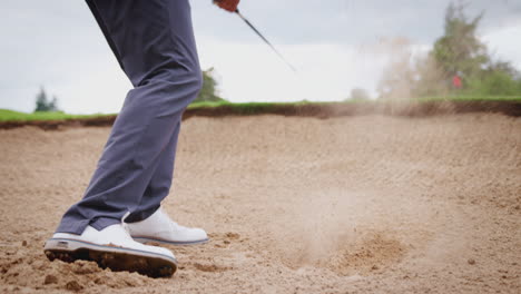 close up of male golfer hitting golf ball out of bunker and onto green